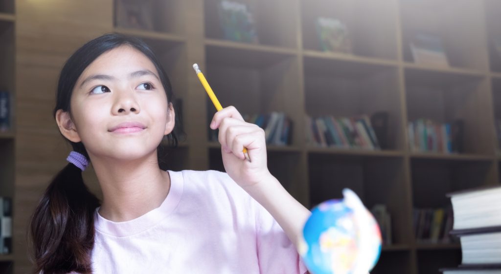 Curious girl with pencil and globe, pondering her educational journey in a cozy library
